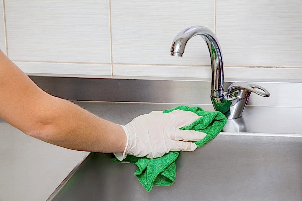 GettyImages 636288996 10 House Cleaning Hacks That Professionals Use 2 Hand in protective glove with rag cleaning commercial kitchen sink